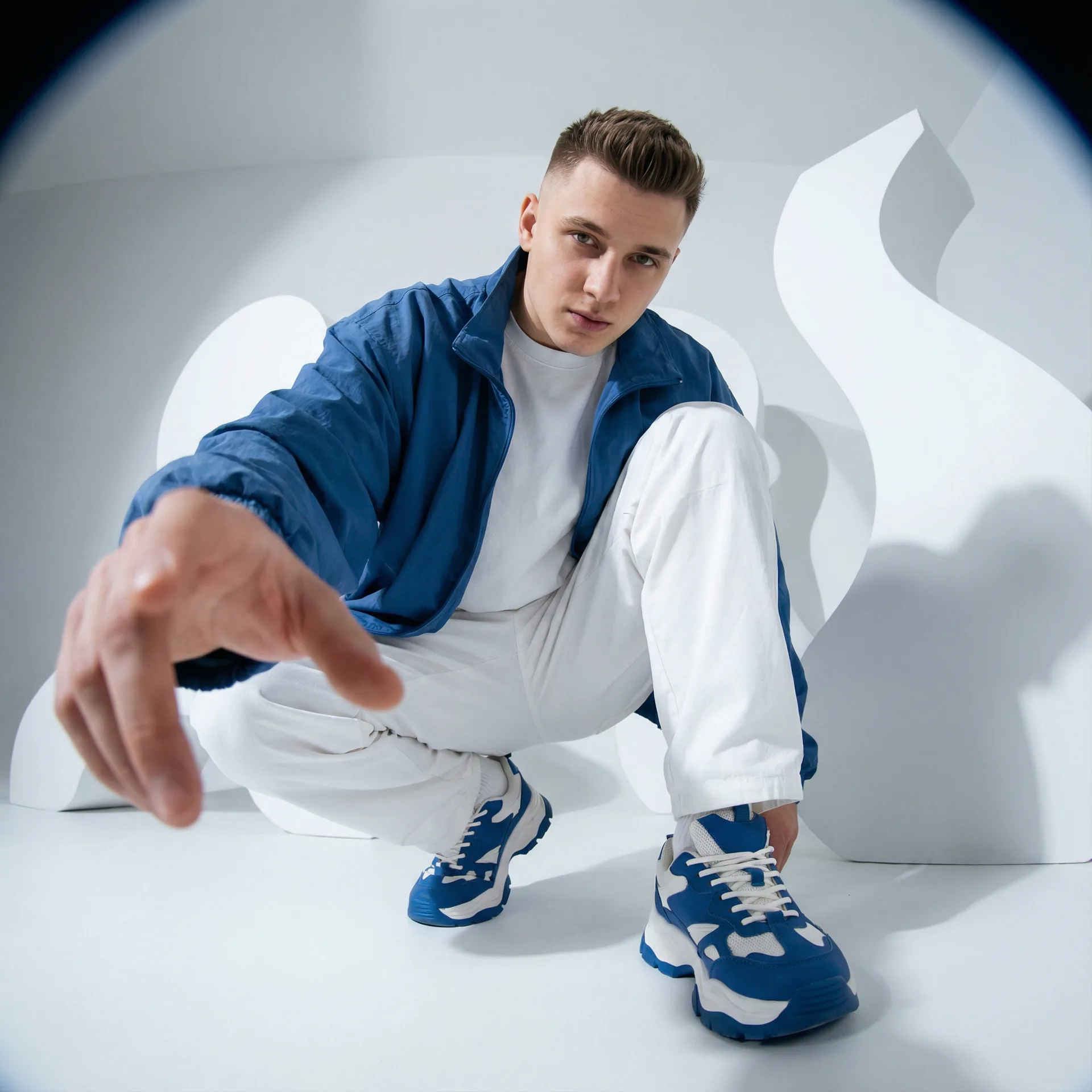 Fashion editorial: young man crouched at a wide-angle lens, hand toward the camera