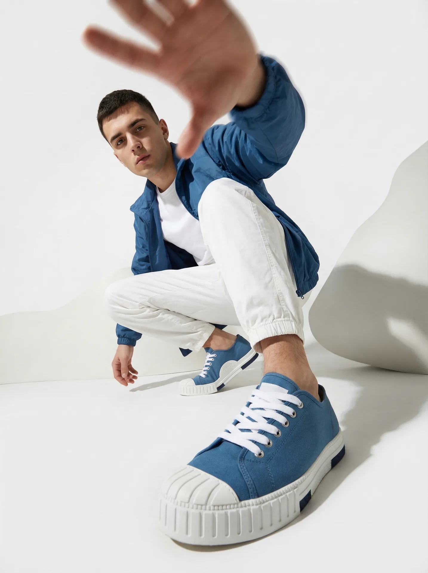 Fashion editorial: young man crouched at a wide-angle lens, hand toward the camera