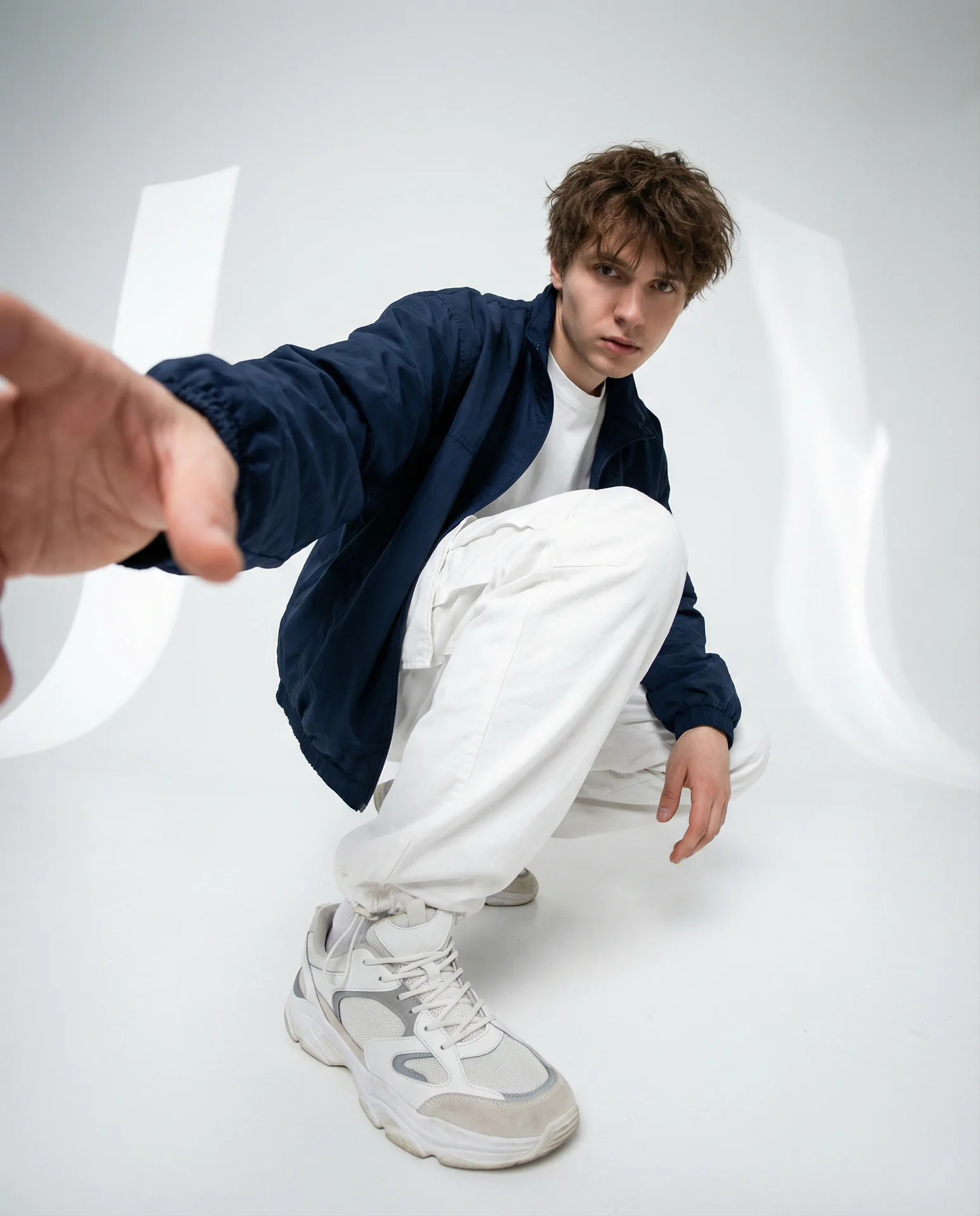 Fashion editorial: young man crouched at a wide-angle lens, hand toward the camera